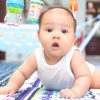 Baby boy on play mat with colorful hanging toys in a nursery.