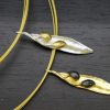 Elegant olive leaf necklaces in gold and silver with black accents on dark wood background.
