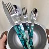 Set of stainless steel cutlery with blue patterned handles in a small bowl.